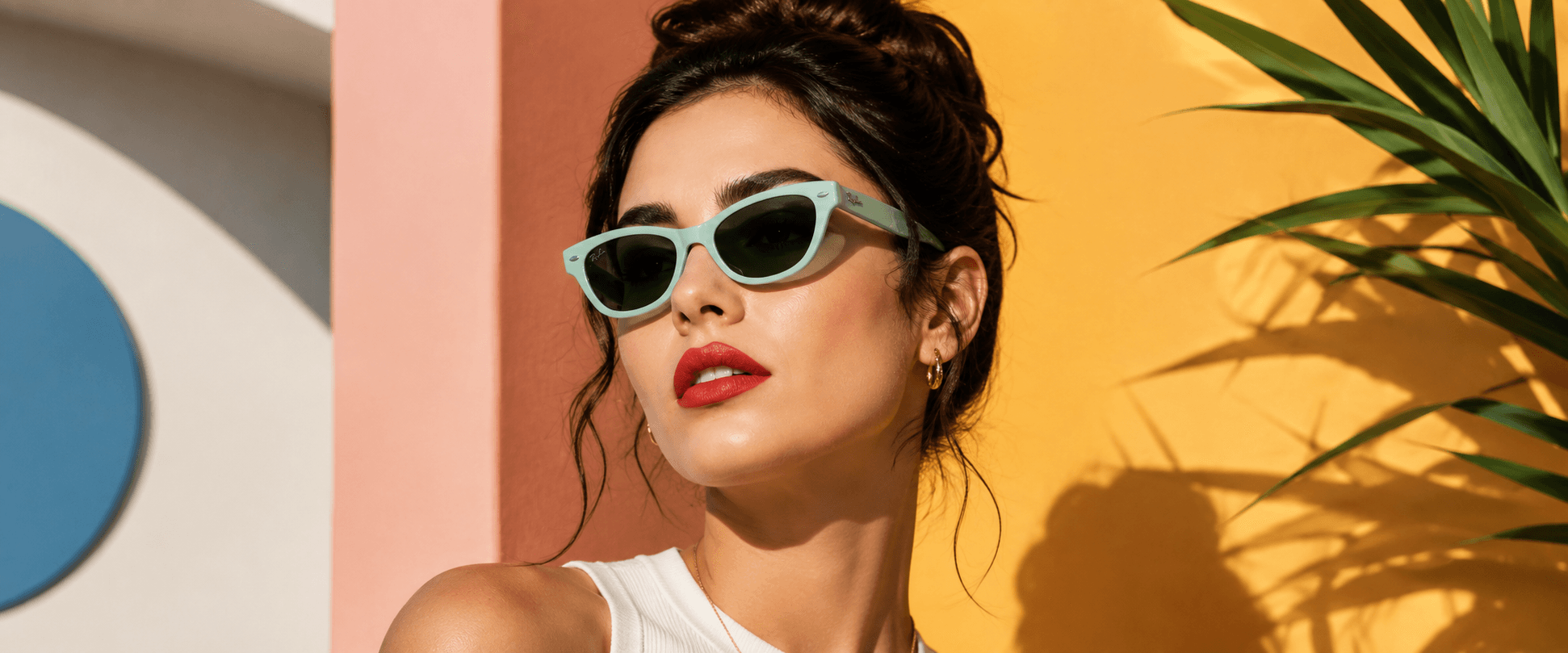 Woman wearing mint cat-eye sunglasses against a colourful pink and yellow wall, Optic Palace